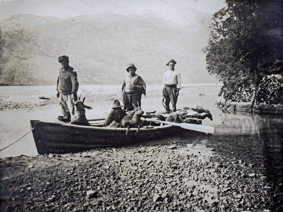 Cuatro trabajadores en un bote sobre un remanso del río Baker, posando con huemules cazados